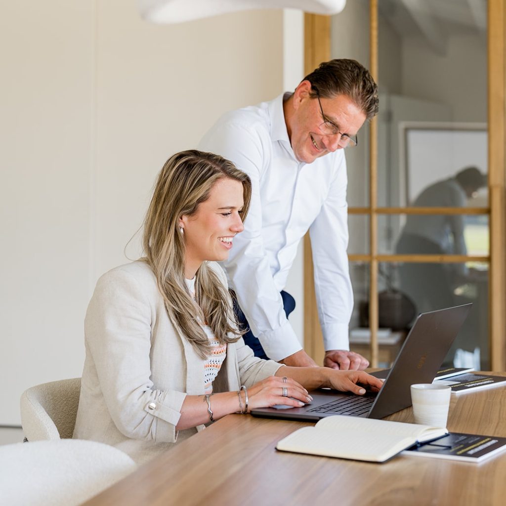 Collega's werken samen op laptop, kantooromgeving.