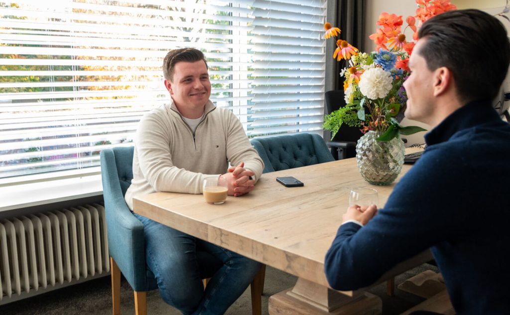 Twee mannen praten aan tafel met bloemenvaas.